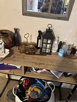 View of wooden shelf with two brass containers with heart-shaped holders, black metal and glass lantern-style lamp, and various bottles and personal products.