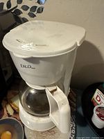 Front view of the white Ekco coffee maker showing the plastic body, brand name, glass carafe with a white handle, and minor stains on the top lid.