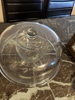 Clear glass cake dome with a knob handle on top, shown inverted on the base on a dark marbled table.