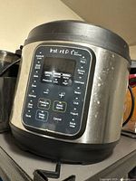 Front view of the Instant Pot Duo Gourmet showing the control panel with various preset cooking functions and visible wear on the stainless steel body.