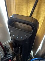 Close-up image of the fan top showing black plastic handle and touch control panel with icons for power, oscillation, speed, and timer.