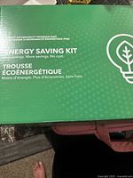Closed green box labeled 'Energy Saving Kit' containing LED lightbulbs inside.