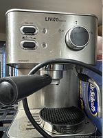 Close-up of Living Basics silver espresso machine front panel with buttons, dial, portafilter, and steam wand.