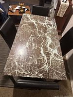 Top view of the rectangular dining table showing brown marble and white veining glass top surface with black legs.