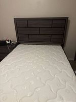 Full view of queen size mattress on bed frame with dark wood headboard, showing the mattress surface and headboard pattern.