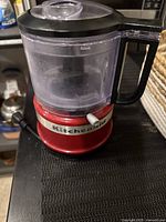 Red KitchenAid mini chopper showing full unit with base, clear container, and black handle on a counter.