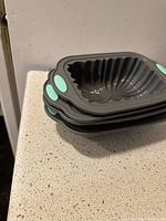 Stacked view of four grey silicone loaf pans showing their unique interior patterns and mint green handles
