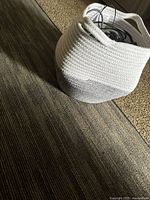 Small white and gray woven storage basket placed on carpet, with visible cables inside basket.