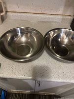 Two stainless steel mixing bowls of different sizes on a kitchen countertop showing signs of use.