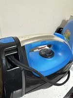 Blue and black clothes iron with silver handle and temperature dial, dusty and worn.