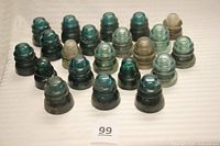 20 glass electrical insulators arranged in groups showing aqua colored glass with some in translucent and light brown hues, various shapes typical of early-to-mid 20th century insulators.