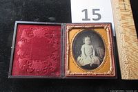 Full view of the open cased daguerreotype showing the toddler seated in a chair with red velvet on the left side of the case.