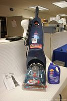 Front view of Bissell Proheat 2X deep cleaning carpet cleaner with user guide and cleaning solution jug beside it.
