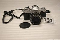 Front angle view of Canon AT-1 35mm film camera with lens and strap. Lens cap also shown, placed separately.