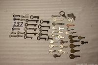 Full layout of the collection of approximately 52 metal keys including skeleton keys and modern keys, laid flat on a beige surface with lot number 137.