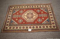 Full view of rectangular Kazak hand-knotted area rug showing primary rust and ivory colors with geometric medallion and border details on carpeted floor.