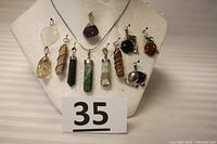 Front view of display bust with all 11 natural rock pendants on silver chain, showing variety of shapes and colors.