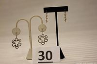 Photo of two sets of earrings displayed on stands, one with open flower shapes and one with leaves wrapped by a silver spiral.