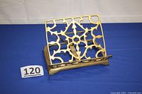 Front view of reticulated brass book holder upright, showing intricate openwork design and adjustable back support.