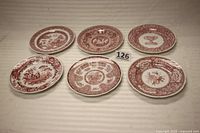 Top-down view of all six Spode plates arranged side-by-side showing distinct patterns and reddish-brown color.