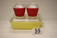 Three vintage Pyrex refrigerator storage dishes: one large yellow dish with clear lid, two smaller red dishes with clear lids stacked on top.