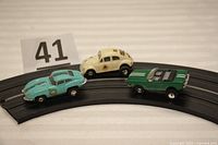 Three slot cars on curved track with lot number sign