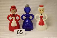 Three vintage female figurine sprinkler bottles side by side showing the different materials and colors.