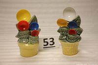 Photo of two porcelain leaf basket measuring spoon holders, one yellow base and one beige base, each with four colored measuring spoons.
