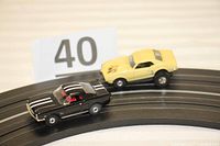 Black Mustang and yellow Firebird on HO scale slot track, front 3/4 view