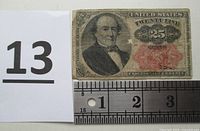 Front side view of worn 25 cent shinplaster note with ruler for scale and lot number.