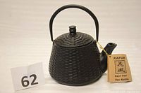 Side view of black cast iron teapot with handle, spout, and Kafuh tag visible.