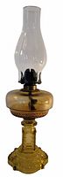 Full view of amber glass kerosene oil lamp showing brass burner, clear glass chimney, and amber glass body and base.