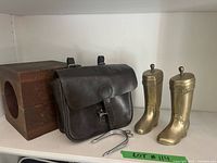 Photo of entire lot showing leather bag, two brass boot bookends, and wooden architectural mould on white shelf