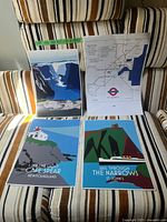 Photo of three art prints on striped fabric: Gros Morne fjords, map of St. John's transit, Cape Spear lighthouse, and The Narrows with a ferry.