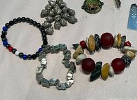 Close-up photo of beaded keychains including black, white, blue, red beads, natural stones, wooden beads, and silver acorn charms