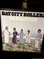 Front cover of Bay City Rollers 'Dedication' vinyl album depicting band members standing outdoors on grass.