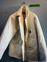 Full front view of white sherpa lined jacket on hanger, showing sherpa lining inside body and collar, and multiple front pockets with snap button closure