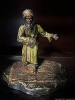 Front angled view of the cold painted bronze sculpture showing the bearded man wearing a turban and yellow robe standing on a decorated carpet base.