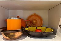 Set displayed inside cabinet shelf showing ceramic teapot with metal bowls and juicer