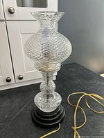 Front view of the clear crystal diamond cut lamp on black wooden base with power cord extending from under.