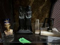 Wide shot showing all five Egyptian themed statues arranged side by side on a shelf under warm light.