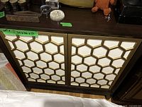 Front view of dark brown wooden cabinet with gold geometric pattern on cream door panels, showing overall design and minor surface wear.