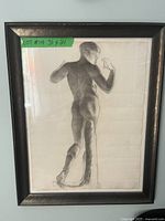 Frontal photo of the framed charcoal drawing showing the human figure from behind, with visible minor edge wear and wrinkles in the paper, inside a black wooden frame.