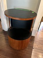 Front view of round wood and black laminate side table showing three wood supports and circular shape.