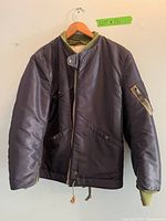 Front view of navy blue and green nylon jacket with zipper and snap button details.