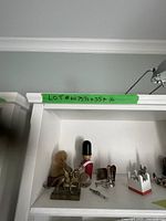 Front view of white wooden shelf unit with assorted small decorative items inside, showing dimensions taped on top edge.