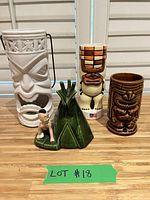 Set of four tiki mugs and one green ceramic figurine on table with daylight, front view showing facial features and designs.