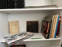 Shelf showing various historical books and maps about Toronto, some hardcover and some paperback. Books and maps show signs of age and wear.