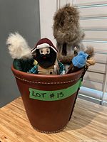 Bucket filled with lumberjack and indigenous dolls made of fabric and fur, showing front view of some dolls inside bucket.