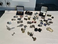 Wide view of multiple pairs of cufflinks arranged on a white surface showing various themes and styles including sports, novelty, and classic.